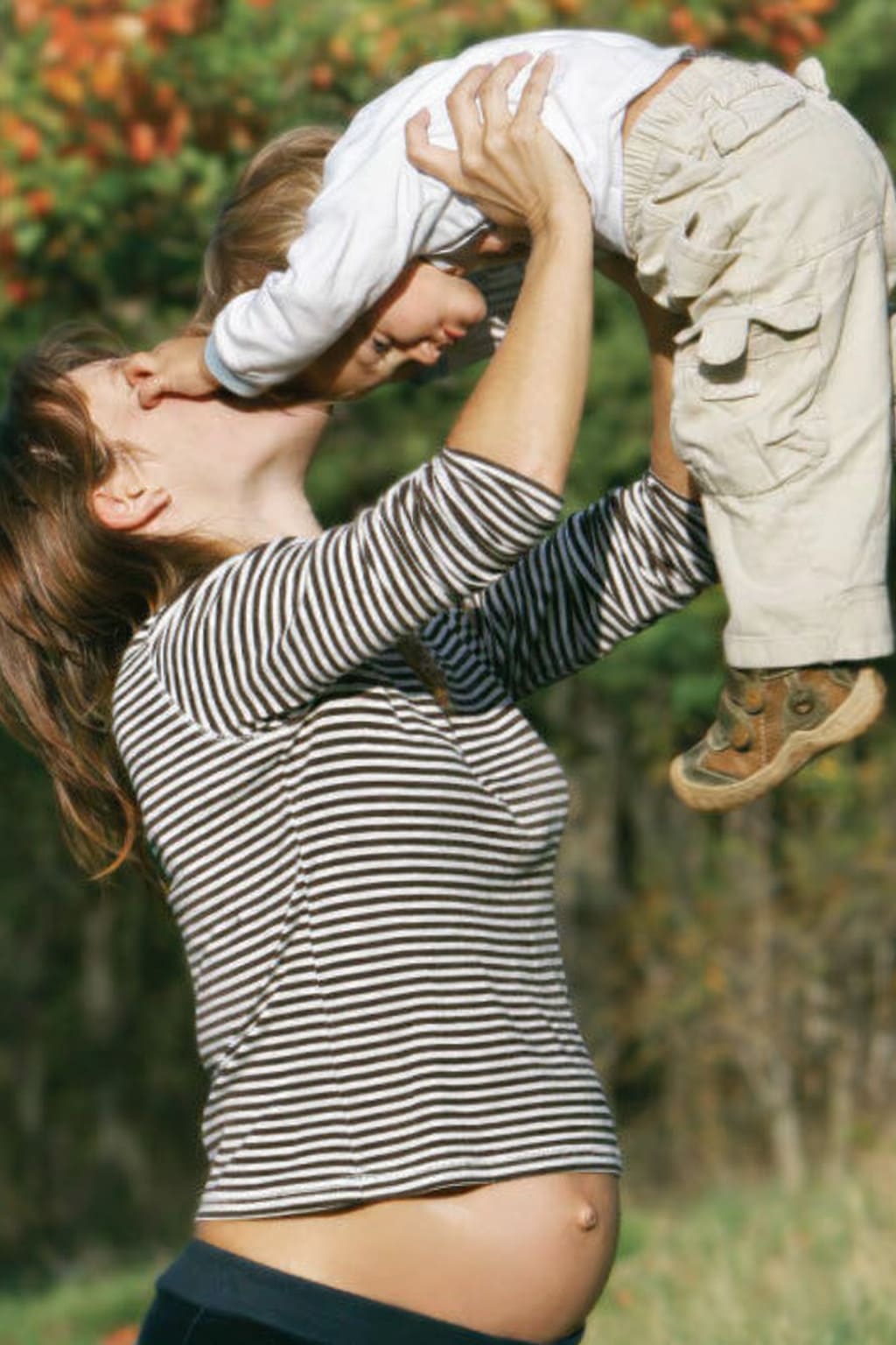 Pregnant mother lifting her child outdoors.