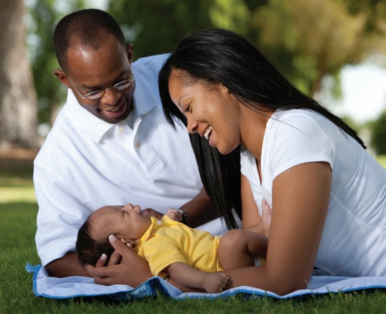 A family with their baby outside on the grass with a blanket