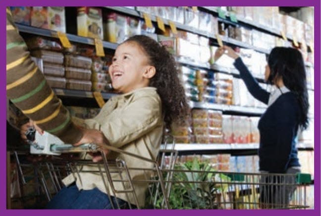 Girl sitting in a shopping cart while adult is shopping