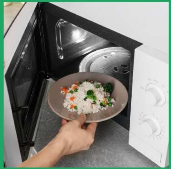 A microwave with rice and fresh vegetables being put in to cook.