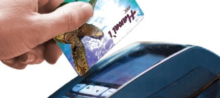 Hand inserting a Hawaii One card with a sea turtle design into a payment terminal.
