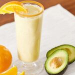 Orange Squeeze Smoothie in a glass with an avocado on the side