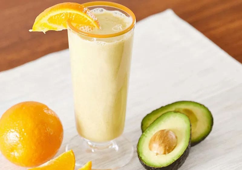 Orange Squeeze Smoothie in a glass with an avocado on the side