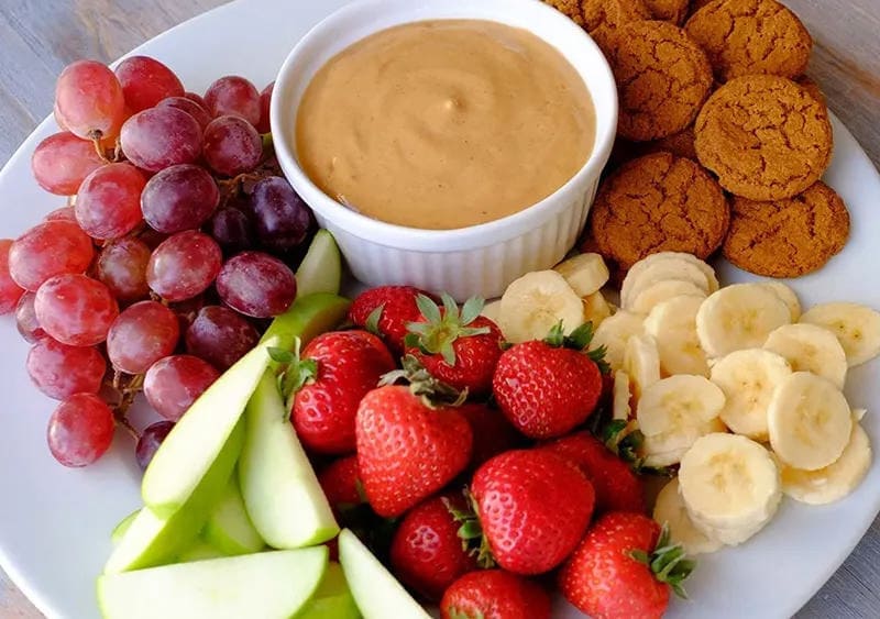 Pumpkin dip in a bowl surrounded by fruits and vegetables
