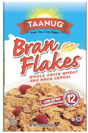 Box of Taanug Bran Flakes cereal with a bright sun graphic, wheat illustration, and raspberries shown with the flakes. Packaging highlights whole‑grain wheat and bran, low fat, cholesterol‑free, and added vitamins and minerals.