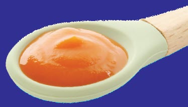 Close‑up of a spoon holding smooth orange baby food against a solid blue background.